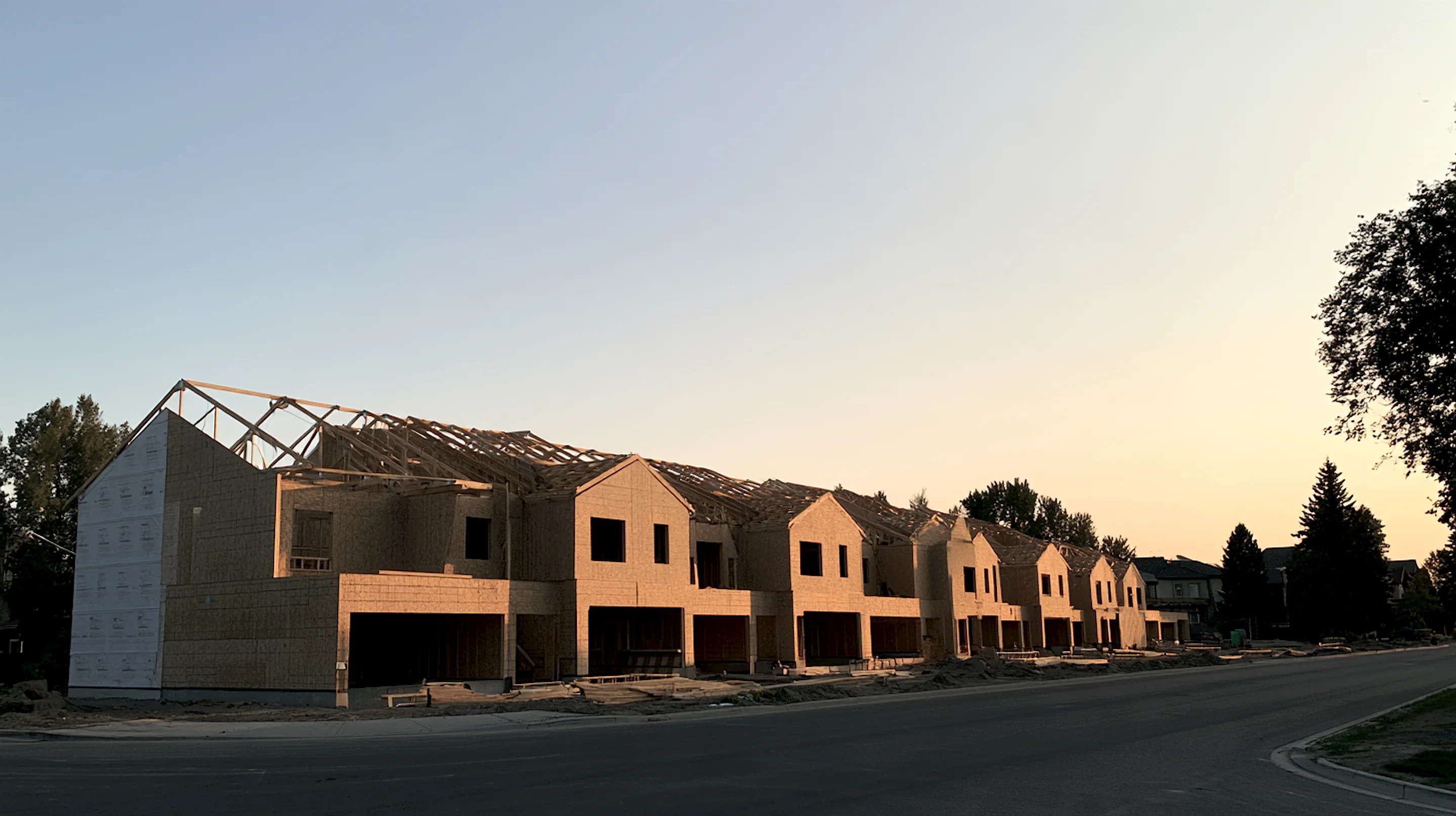 A row of attached two-storey townhomes under construction, roof trusses set